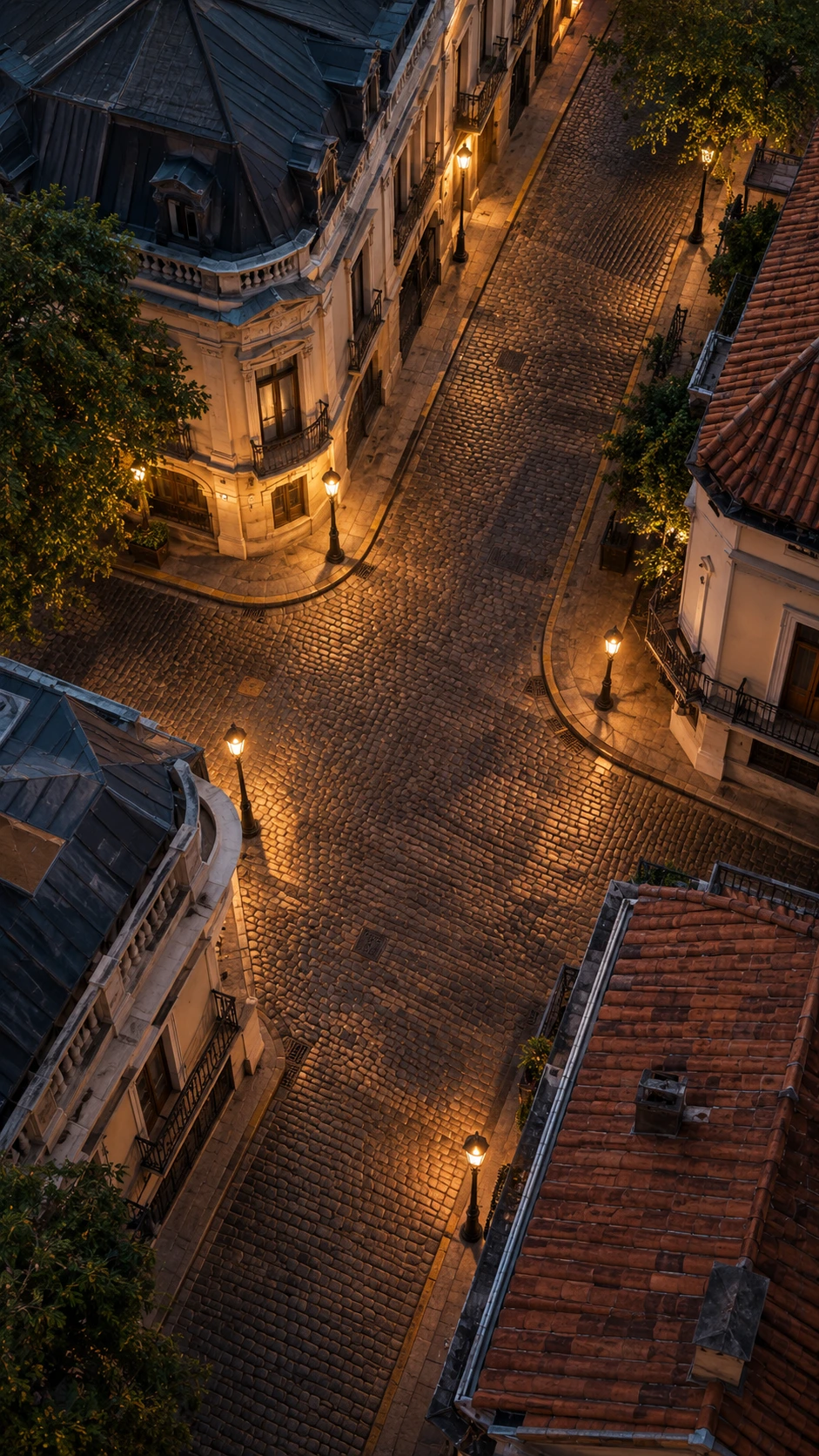 Averiguación de actividades en barrio patrimonial: el dato que ordena todo el proyecto Vista aérea de una esquina adoquinada en un barrio histórico al anochecer, con faroles encendidos, edificios afrancesados con mansardas, techos de teja y árboles que bordean las veredas.