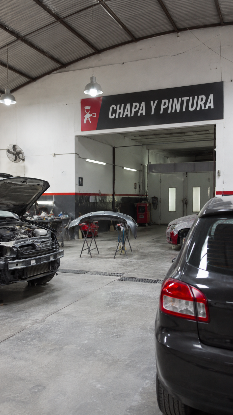 Espacio profesional para reparación de carrocerías y terminaciones en Buenos Aires Interior de taller mecánico con vehículos en reparación, cartel de chapa y pintura, cabina de pintura industrial, herramientas especializadas y espacio de trabajo organizado para restauración automotriz